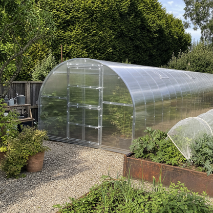 The Classic 9.8 ft wide by 39.4 ft long twin-wall polycarbonate greenhouse stretching along a gravel path beside raised garden beds